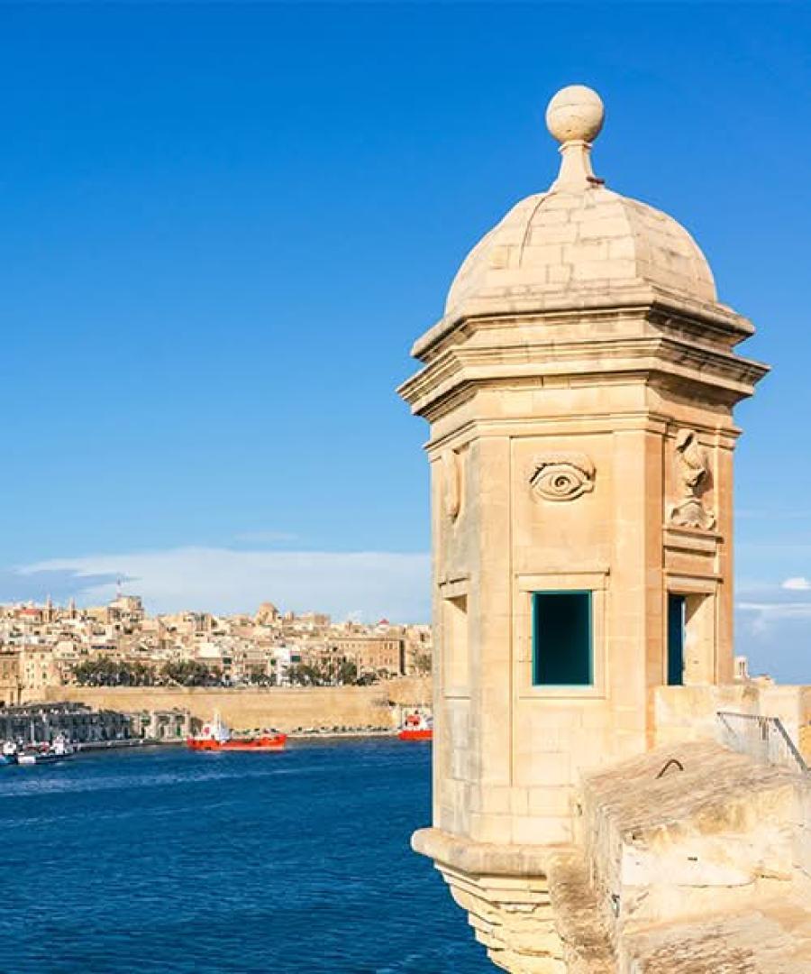 The iconic stone watchtower at Gardjola Gardens in Senglea featuring a sculpted eye on the side, overlooking the blue water.