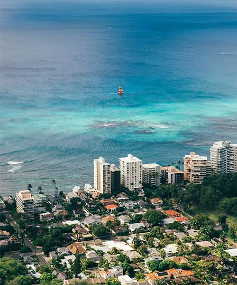 Aerial view of the coastline featuring turquoise waters, a sailboat, and beachfront hotels.