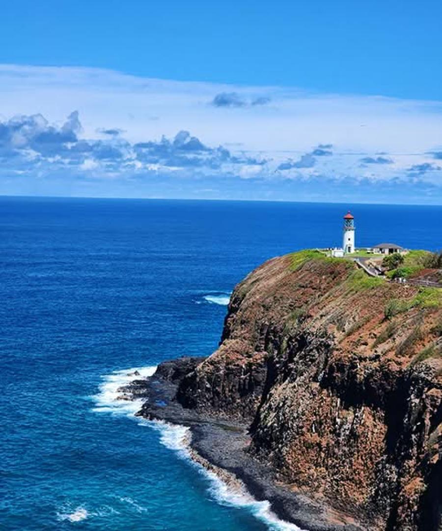Scenic view of the Kilauea Lighthouse standing on a grassy cliff overlooking the deep blue ocean.