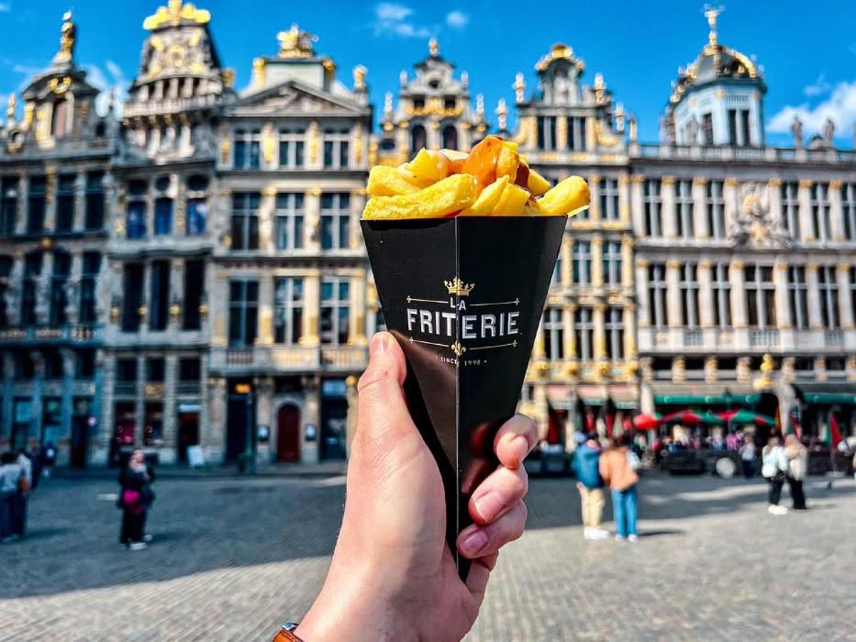 Hand holding Belgian fries in front of historic European buildings