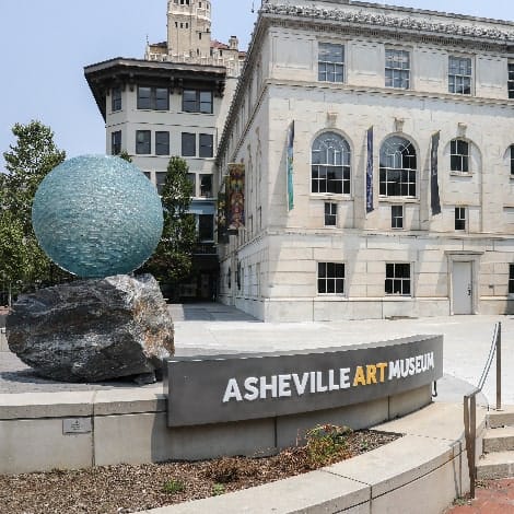 The Asheville Art Museum, showing building entrance, public space, sign, and glass ball and rock sculpture.